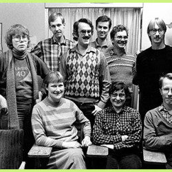 A black and white group photo of people, three of them sitting in the front, others standing behind them.